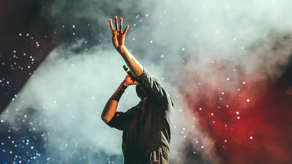 Artista levantando el brazo entre humo de colores sobre el escenario